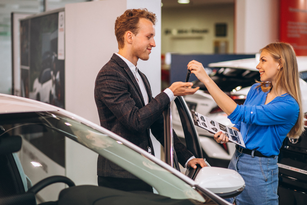 como financiar carro - mulher loira vendedora de veículos entregando chave de carro para um homem
