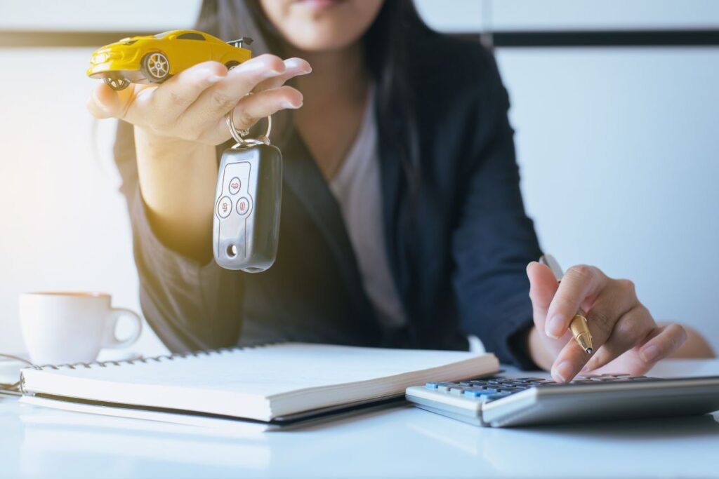 Por que os carros estão tão caros? 8 por que os carros estão tão caros - mulher segurando chave na mão e um carrinho de brinquedo amarelo e fazendo contas
