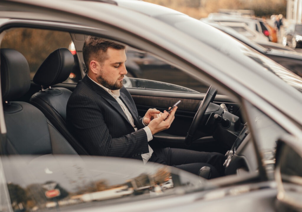 cooperativa de seguro - homem dentro de carro mexendo no celular e com expressão pensativa